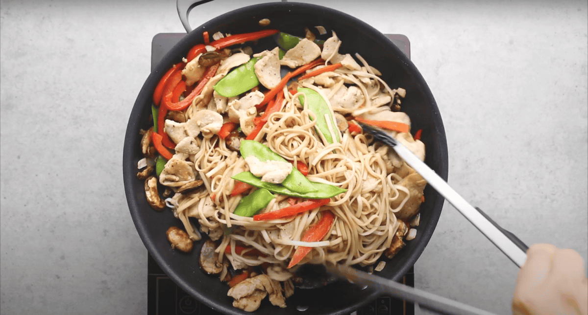 Cooking chicken lo mein in a skillet.