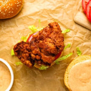 an open-faced spicy chicken sandwich on parchment.