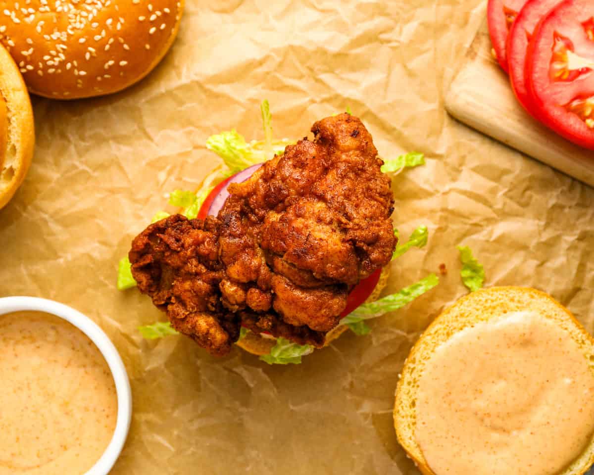 an open-faced spicy chicken sandwich on parchment.