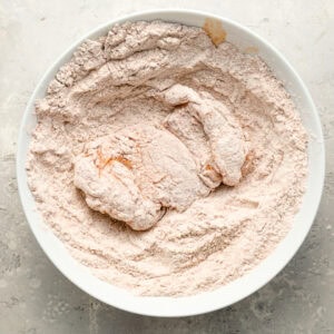 dredging chicken in seasoned flour in a white bowl.