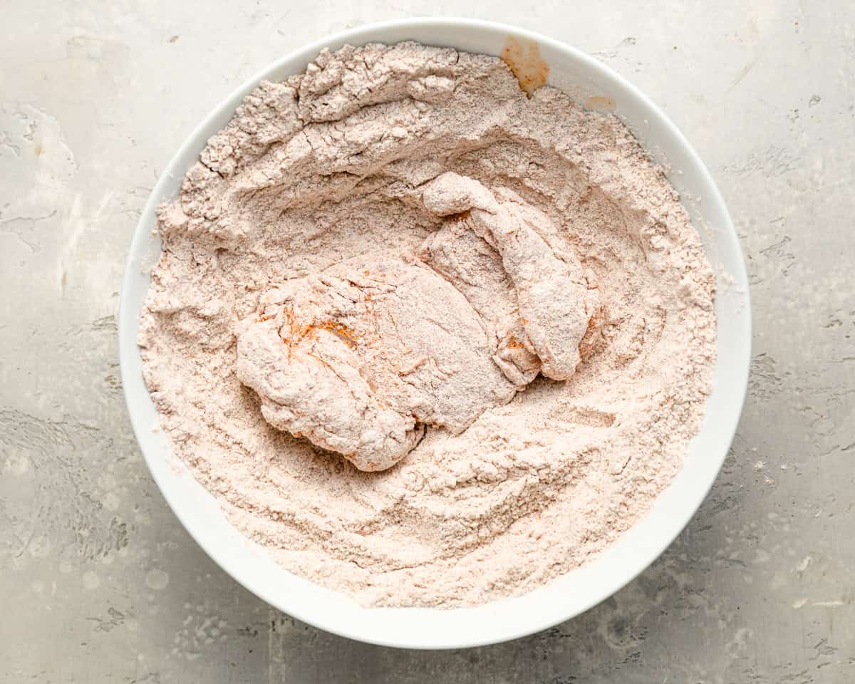 dredging chicken in seasoned flour in a white bowl.