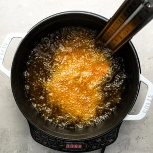 deep frying a chicken thigh in a dutch oven.