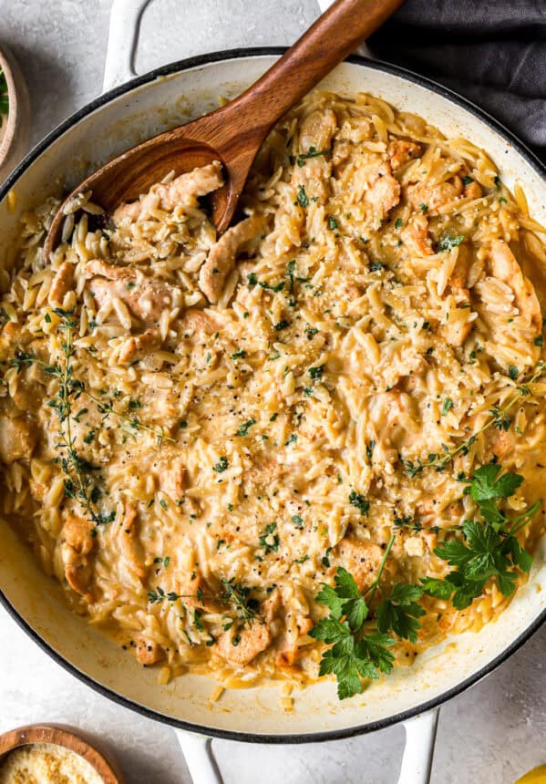 overhead view of creamy chicken orzo in a pan with a wooden spoon.