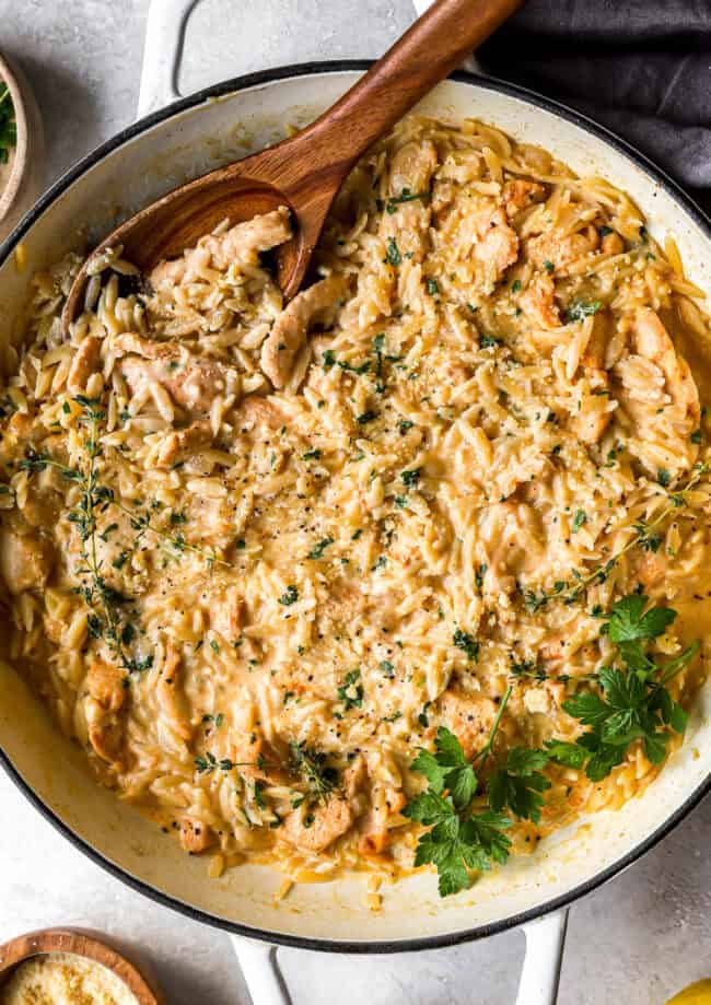 overhead view of creamy chicken orzo in a pan with a wooden spoon.