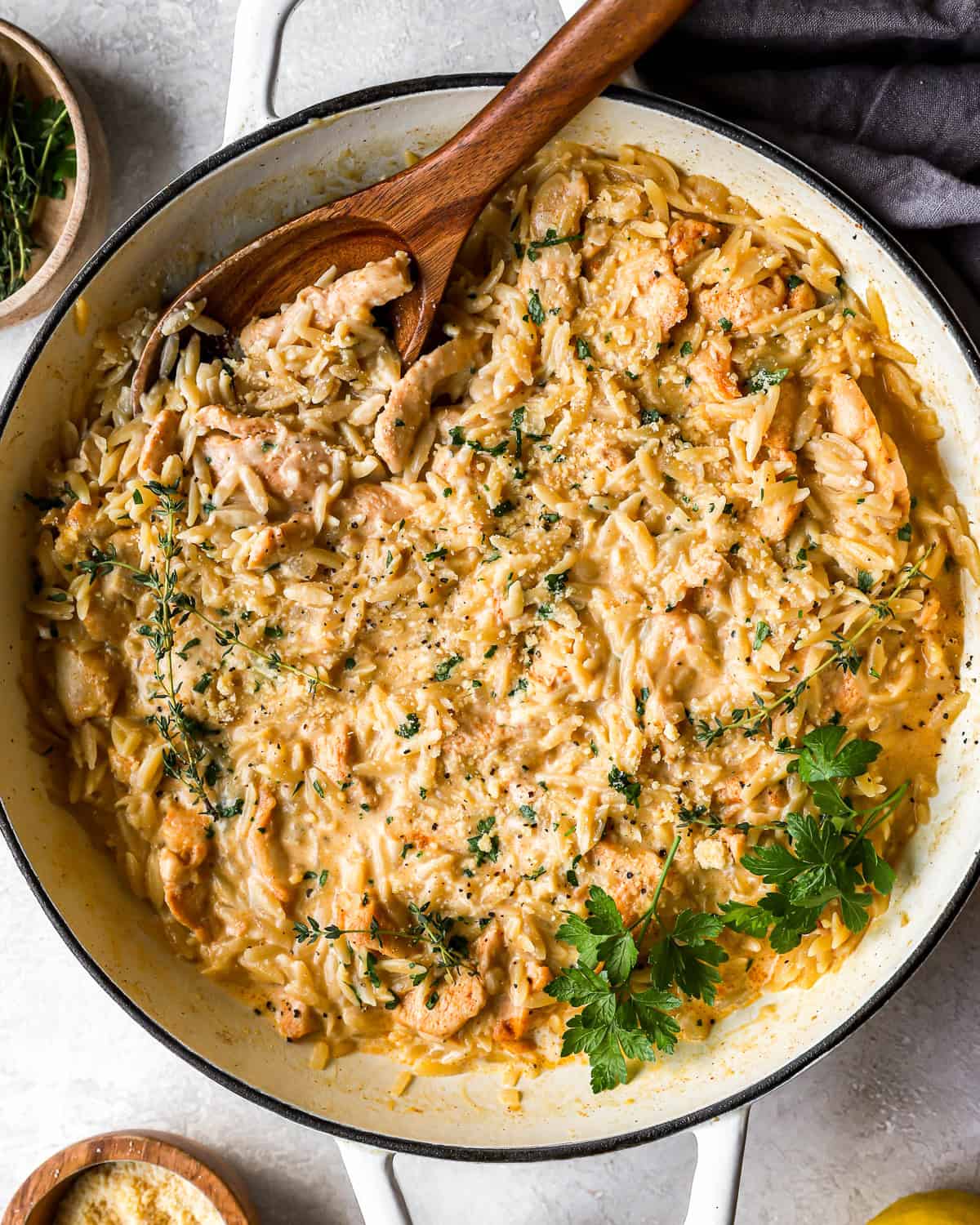 overhead view of creamy chicken orzo in a pan with a wooden spoon.