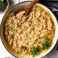 overhead view of creamy chicken orzo in a pan with a wooden spoon.