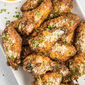 overhead view of baked garlic parmesan chicken wings on a white platter with yellow sauce.