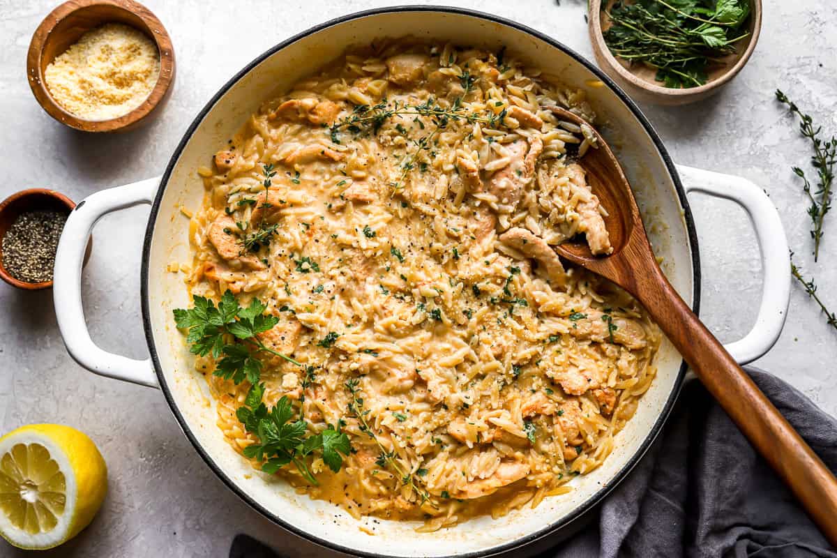 creamy chicken orzo in a pan topped with cheese.