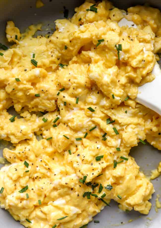 closeup of scrambled eggs in a pan with a rubber spatula.