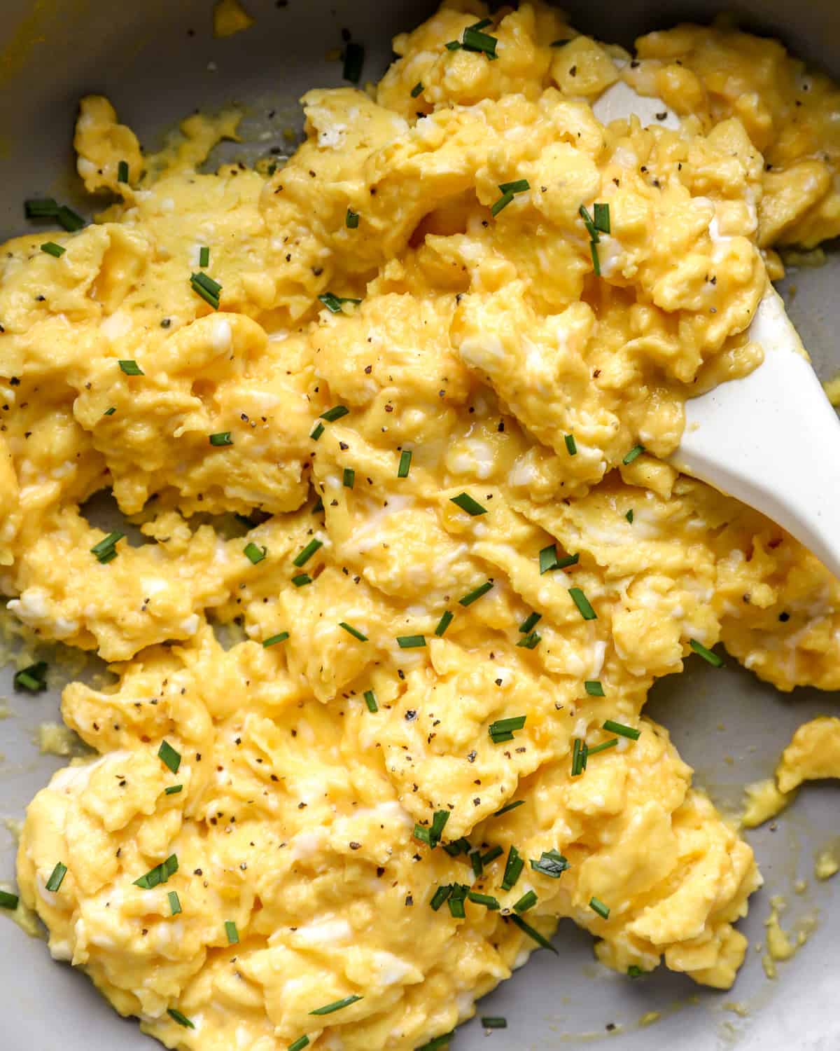 closeup of scrambled eggs in a pan with a rubber spatula.