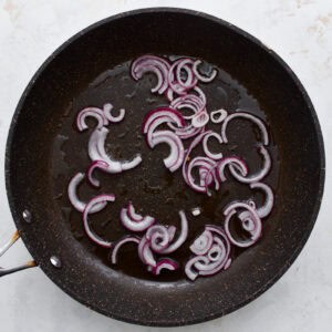 thinly sliced red onion cooking in a pan.