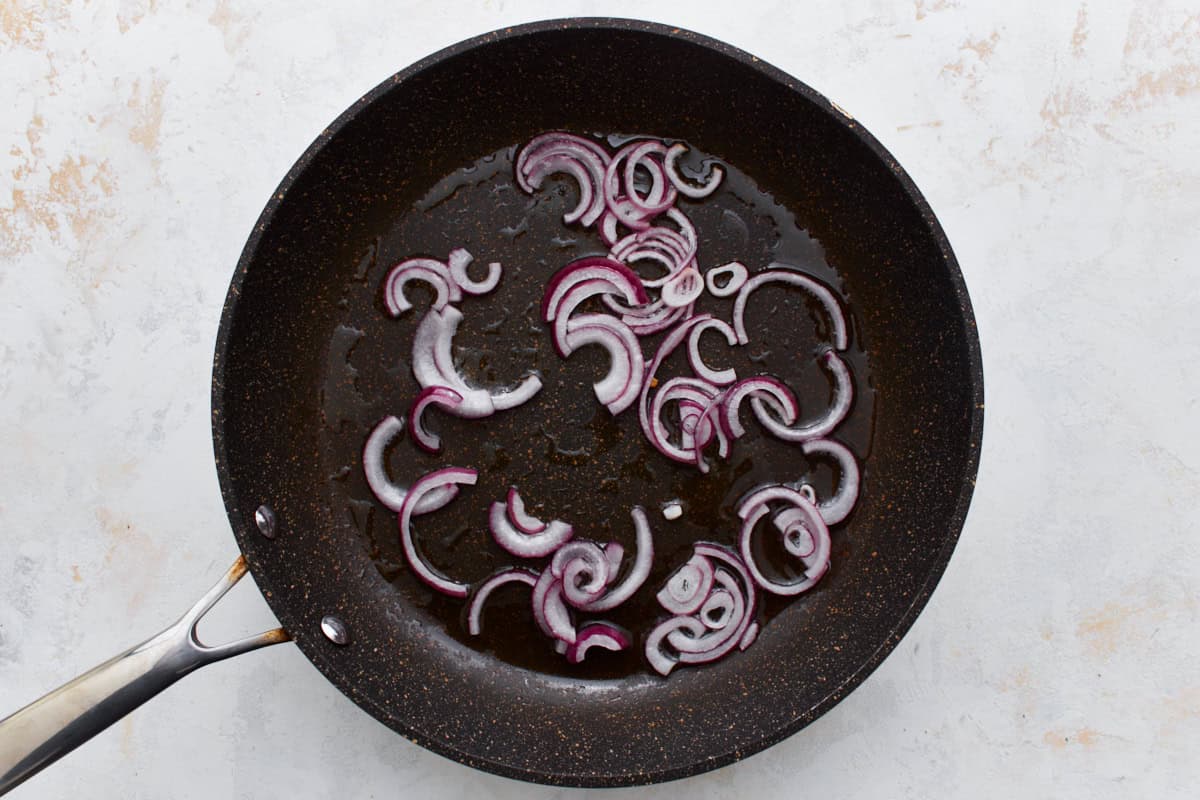 thinly sliced red onion cooking in a pan.