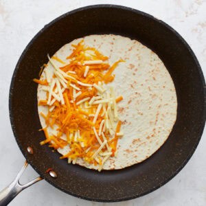 shredded cheese sprinkled over half of a flour tortilla in a pan.