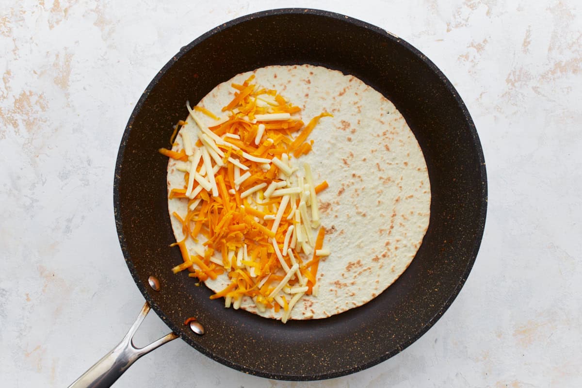 shredded cheese sprinkled over half of a flour tortilla in a pan.