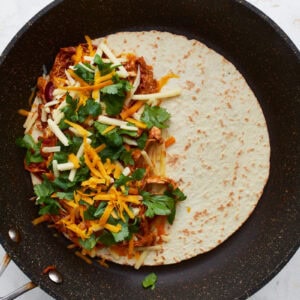 bbq chicken, cilantro, and cheese on half of a flour tortilla in a pan.