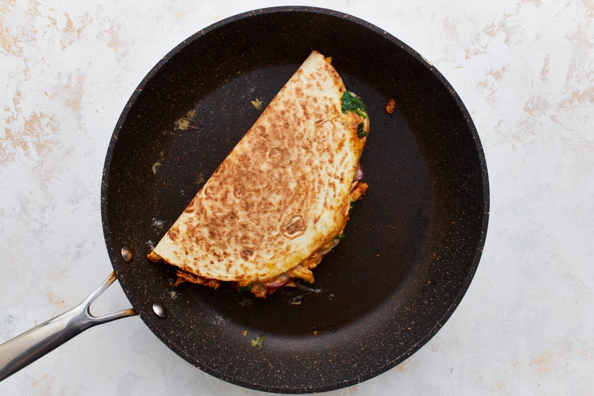 a cooked folded half-moon quesadilla in a pan.