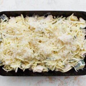 chicken zucchini casserole filling topped with shredded cheese in a baking dish.