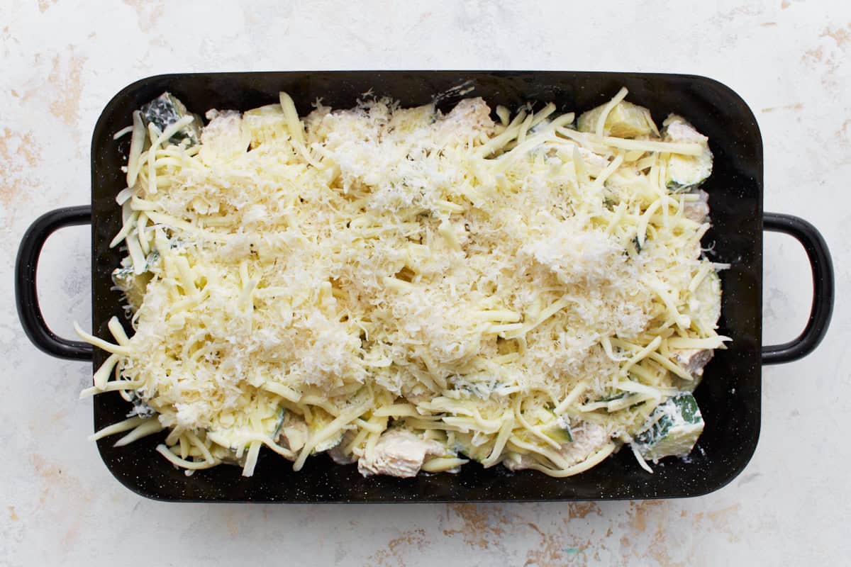 chicken zucchini casserole filling topped with shredded cheese in a baking dish.