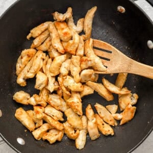 Strips of chicken cooking in a skillet.