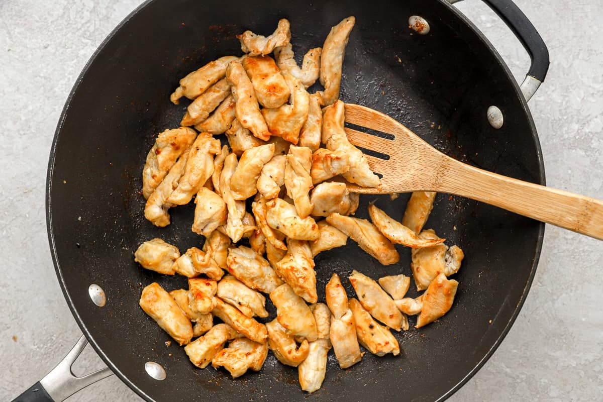 Strips of chicken cooking in a skillet.