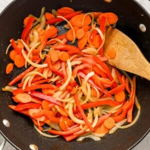 Carrots, onions, and bell peppers cooking in a skillet.