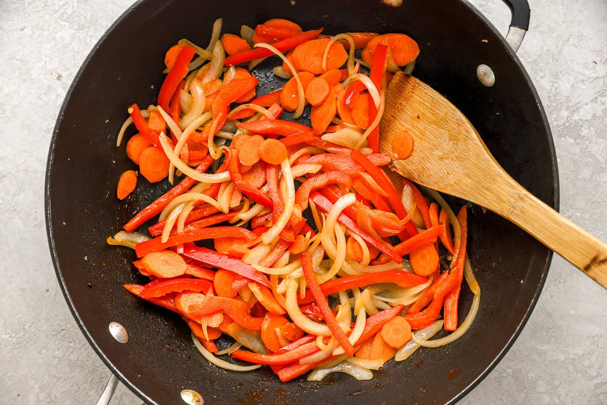 Carrots, onions, and bell peppers cooking in a skillet.