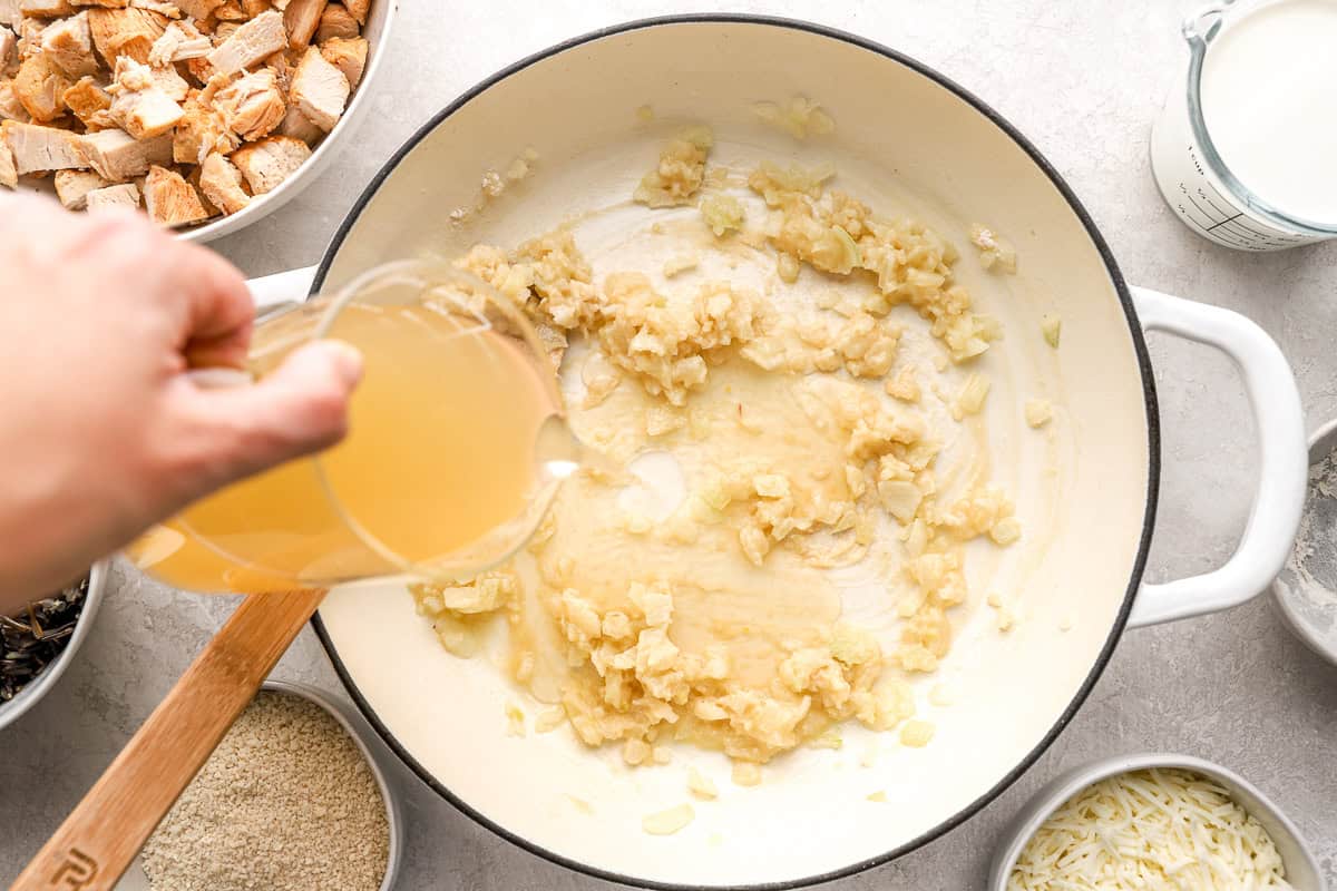 Pouring broth into a pot of garlic and onions.