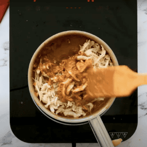 Stirring shredded chicken into mole sauce.