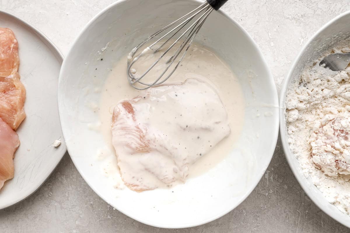 Coating a piece of chicken in batter.