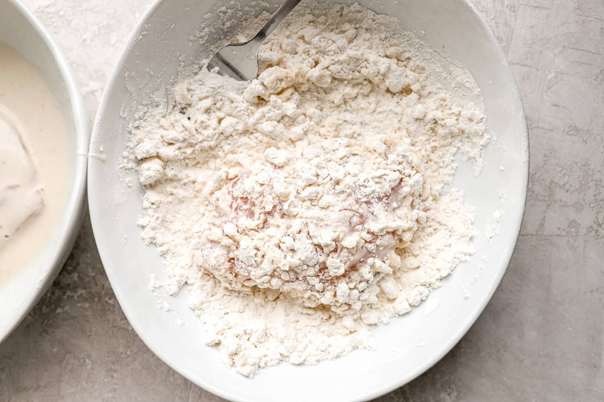 Dredging a piece of chicken in flour.