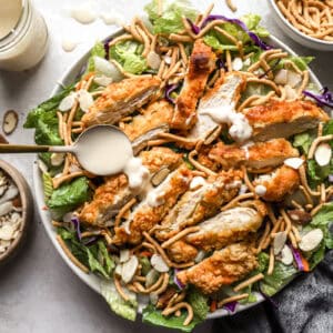 Drizzling dressing on top of a salad with crispy chicken and dried noodles.