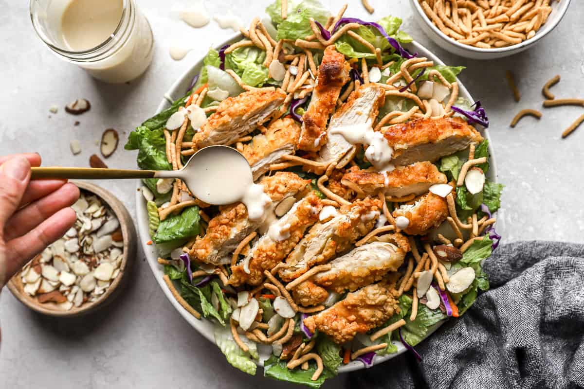 Drizzling dressing on top of a salad with crispy chicken and dried noodles.