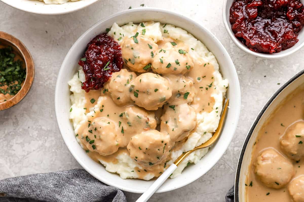 A bowl of chicken Swedish meatballs served over mashed potatoes with lingonberry jam.