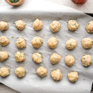 Uncooked chicken meatballs on a baking tray lined with parchment paper.