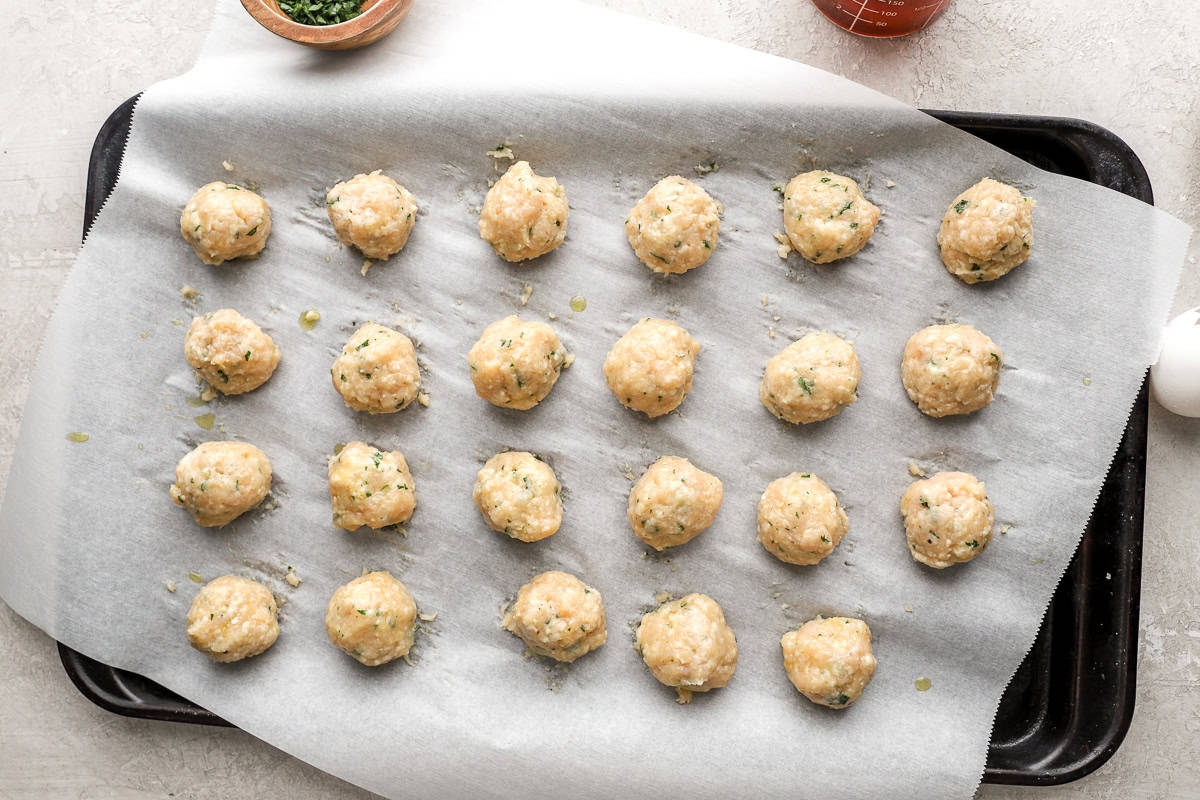 Uncooked chicken meatballs on a baking tray lined with parchment paper.