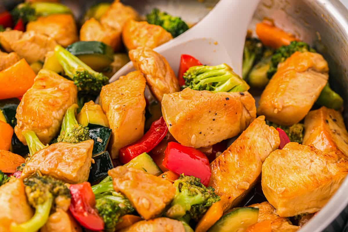 closeup of honey soy chicken stir fry in a pan with a spoon.