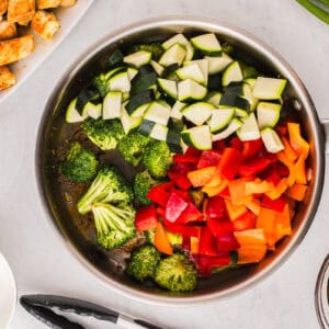 broccoli florets, zucchini, and peppers in a pan.