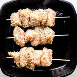 Breadcrumb-coated pieces of chicken on skewers, lined up on a grill pan.