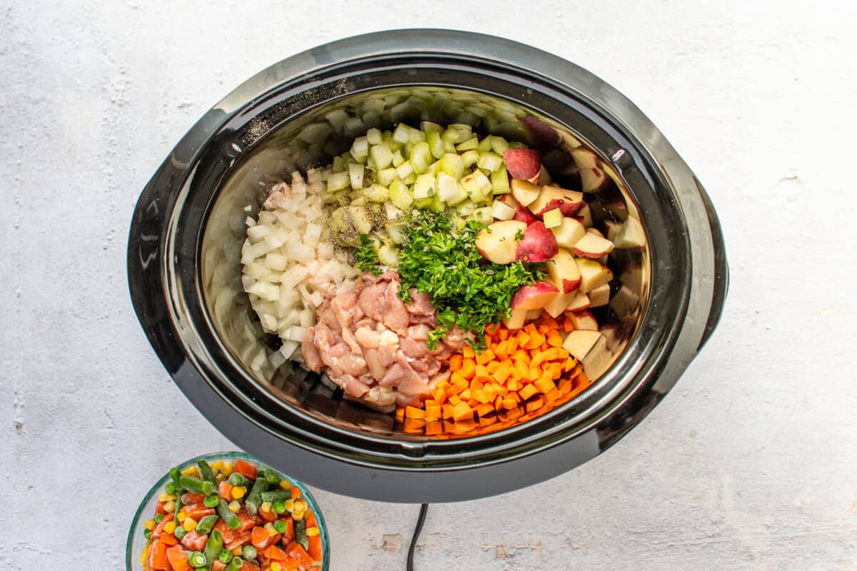 Crockpot filled with diced veggies and chicken.