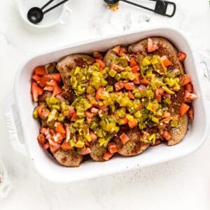 Chicken breasts in a baking dish, topped with chopped tomatoes and jalapeños.