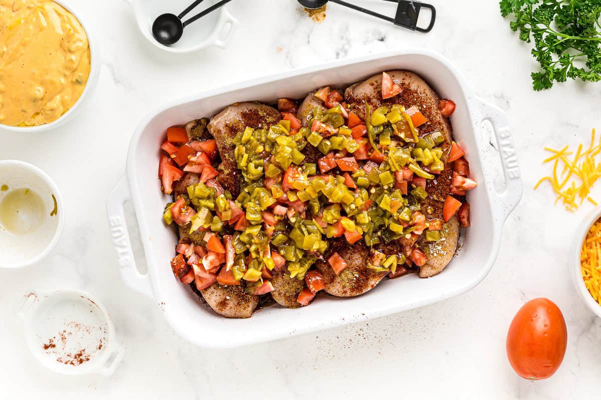 Chicken breasts in a baking dish, topped with chopped tomatoes and jalapeños.