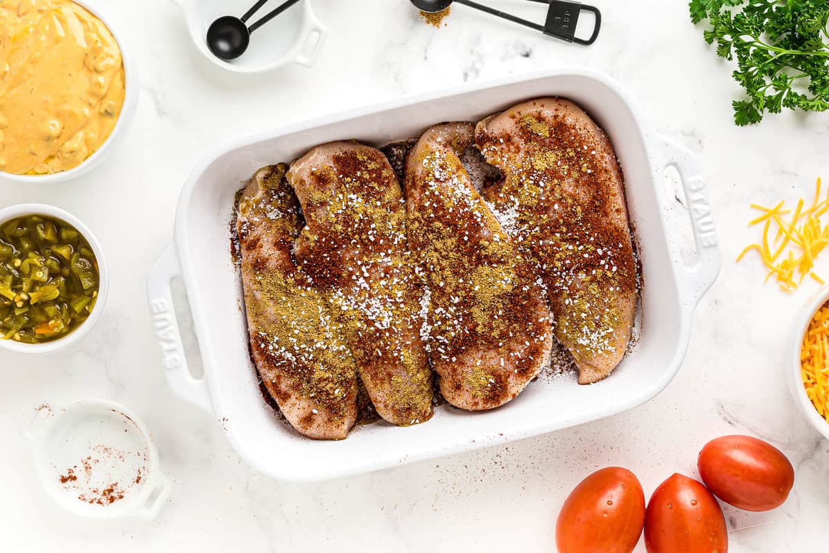 4 chicken breasts in a baking dish, covered with a variety of spices.