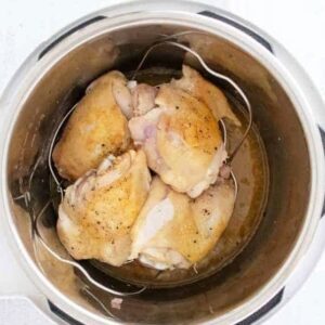 Chicken thighs stacked on top of a trivet inside of a pressure cooker.