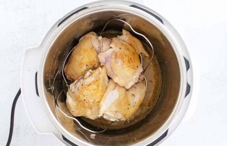 Chicken thighs stacked on top of a trivet inside of a pressure cooker.