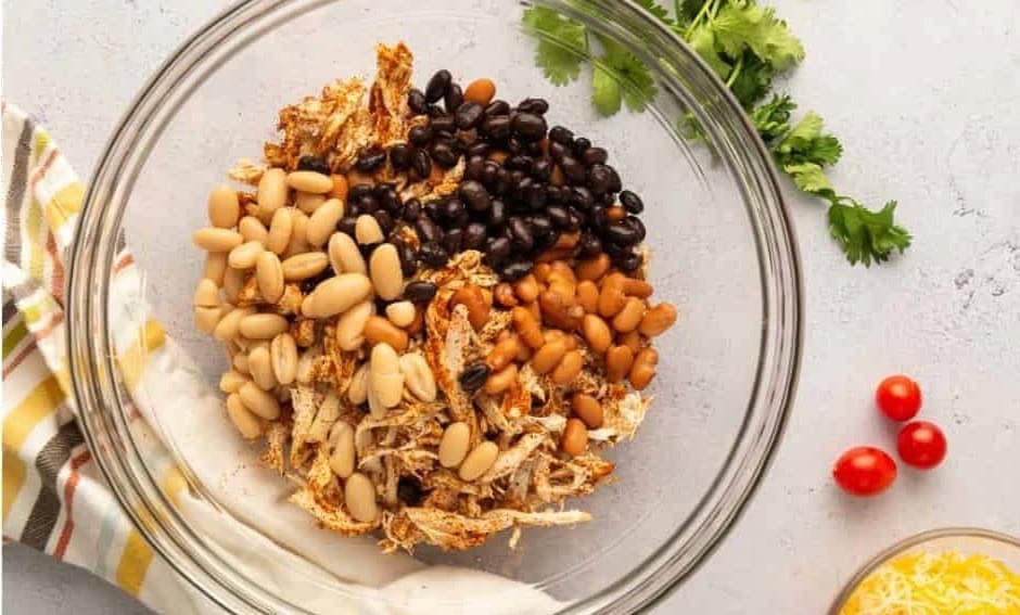 Shredded chicken and beans in a glass mixing bowl.