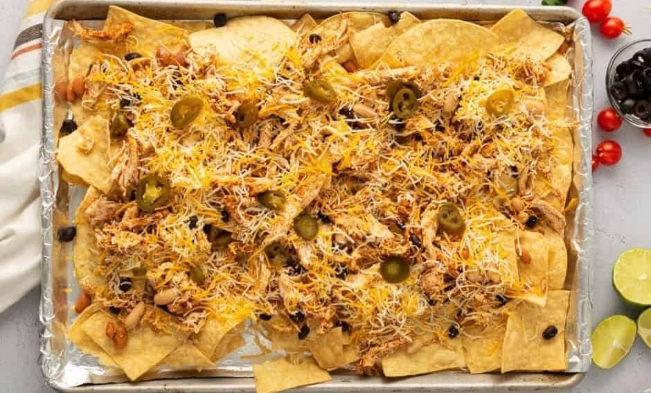 Baking tray of tortilla chips topped with chicken, beans, cheese, and jalapeños.