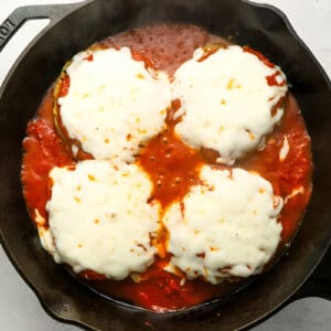 four chicken burger patties topped with marinara and melted cheese in a cast iron pan.