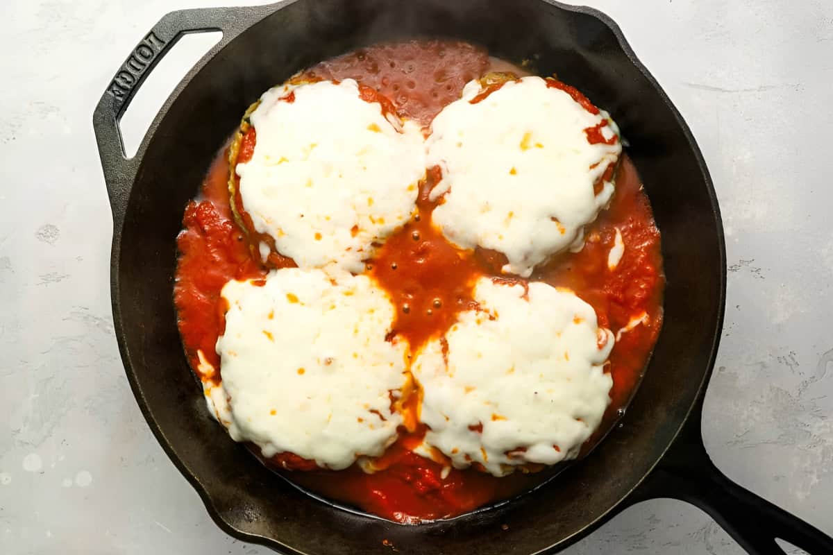 four chicken burger patties topped with marinara and melted cheese in a cast iron pan.