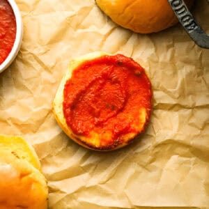 a bottom bun topped with marinara sauce on parchment.