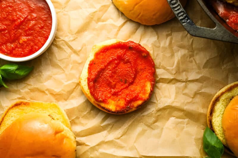 a bottom bun topped with marinara sauce on parchment.